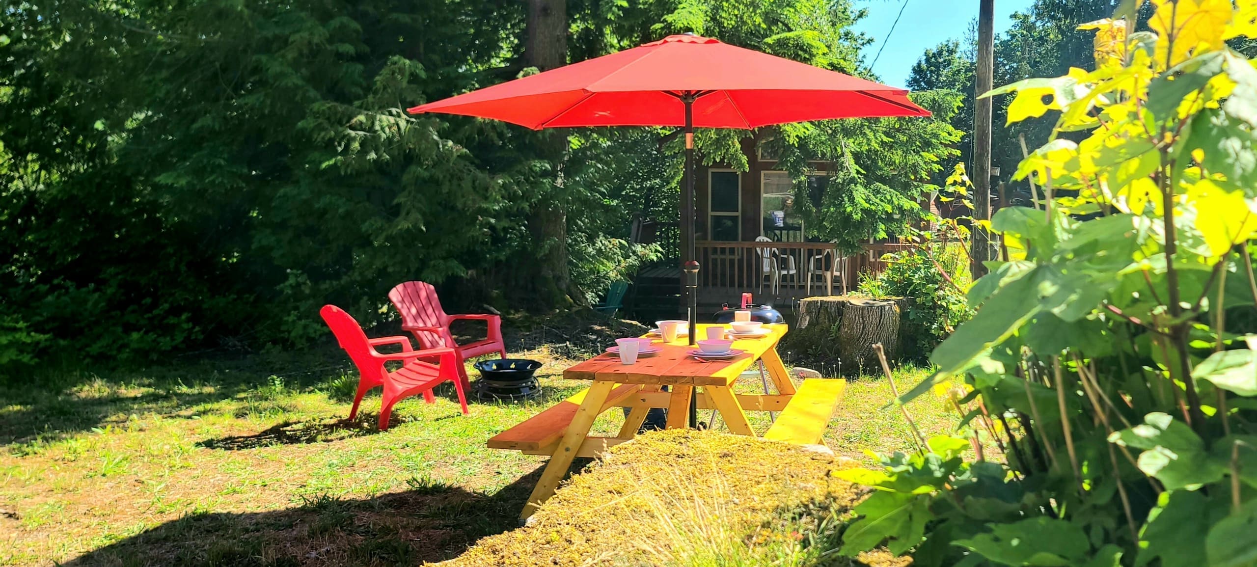Glamping site with a red patio umbrella, picnic table, and chairs beside a cabin