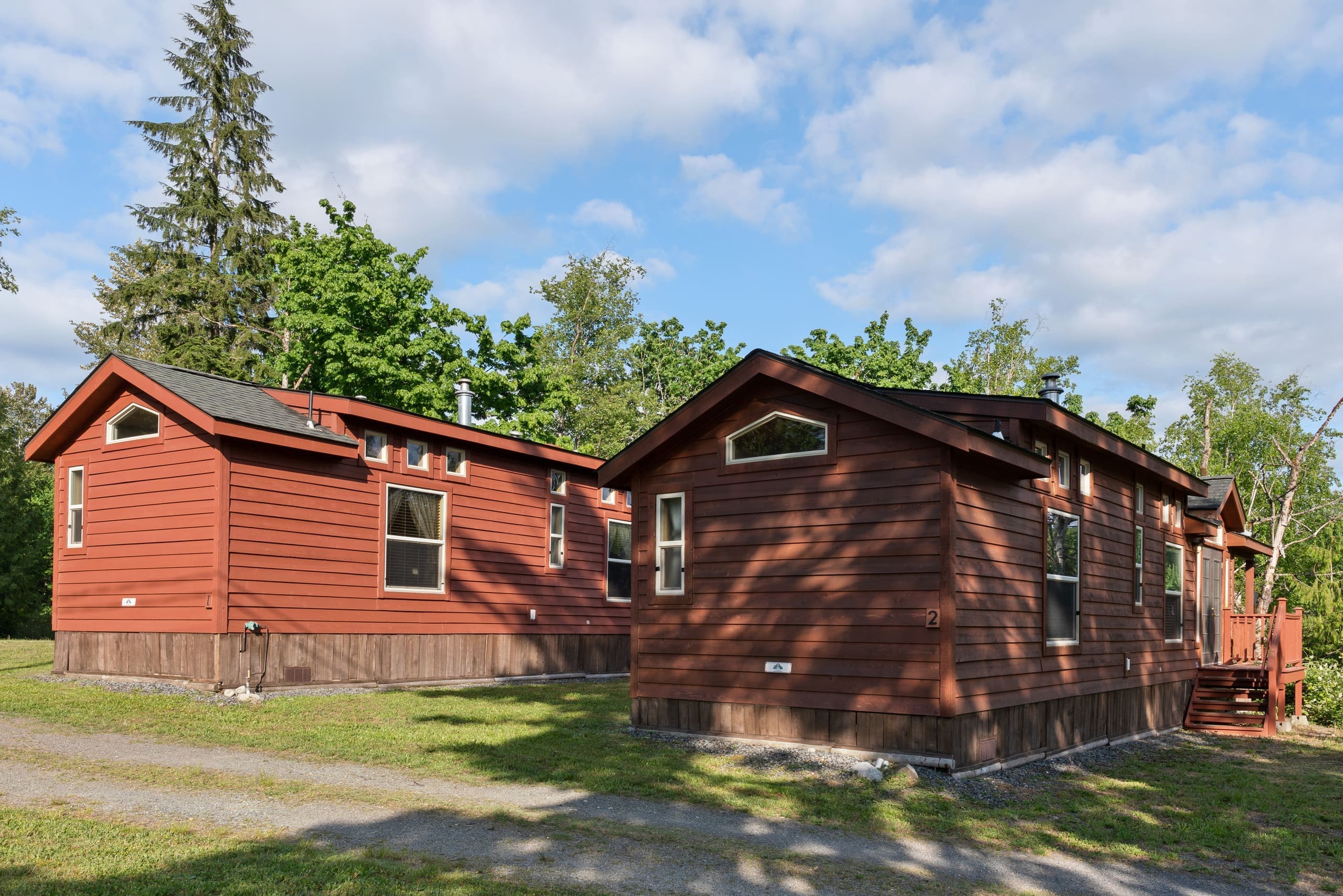 Two red cedar cabins side by side under tall evergreens