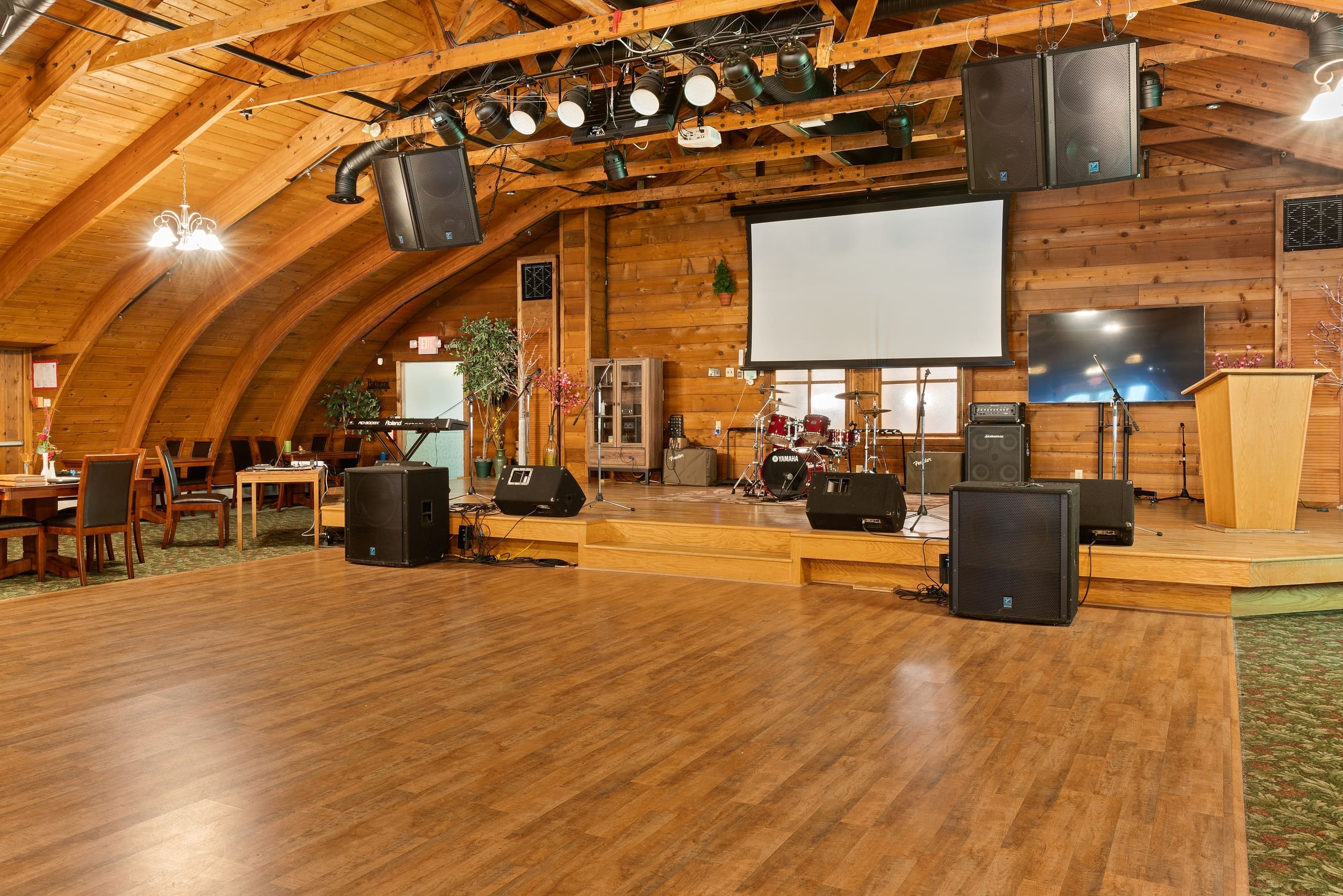 Event hall stage with drum kit, projector screen, and dance floor