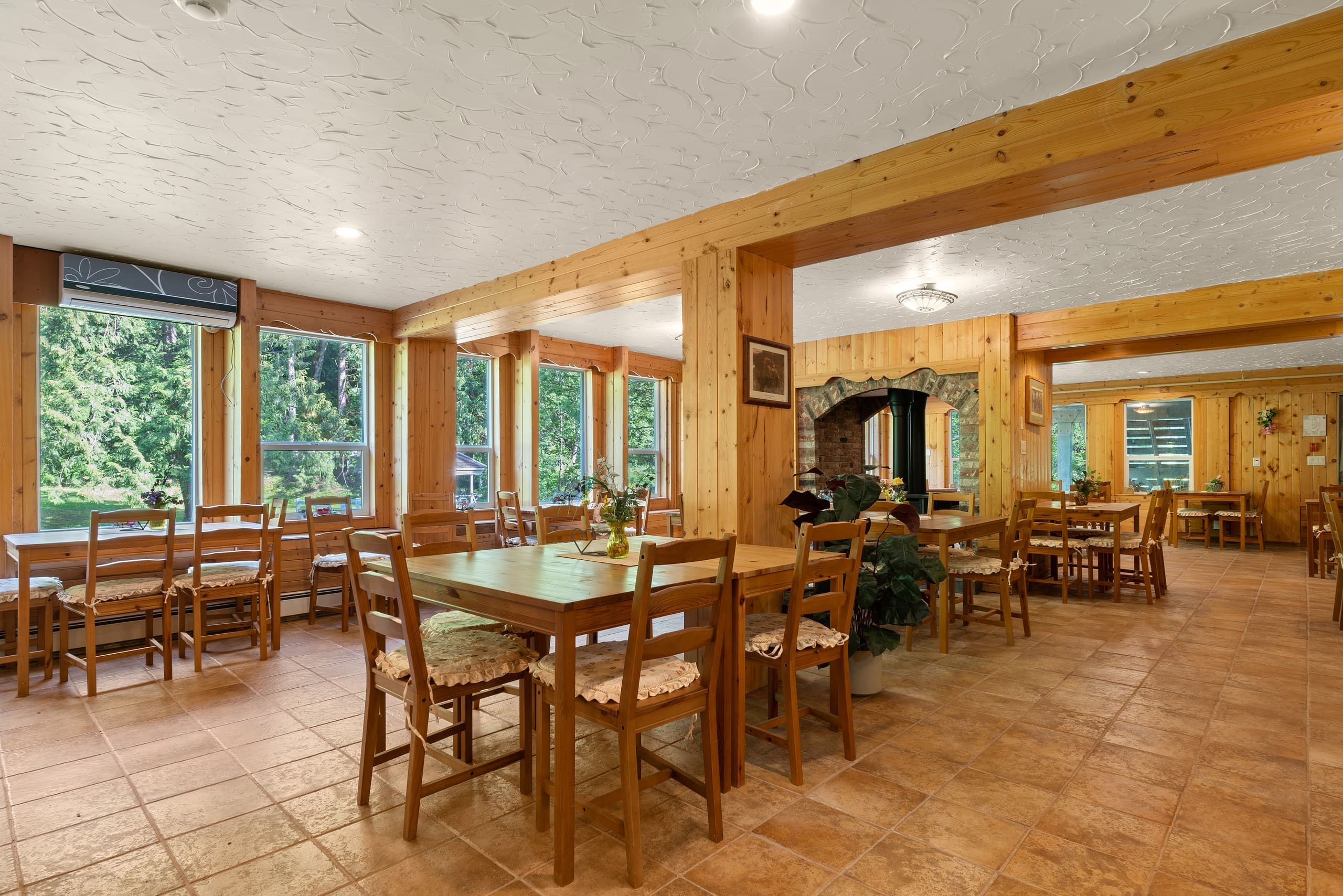 Dining hall with wooden tables beside large forest-view windows