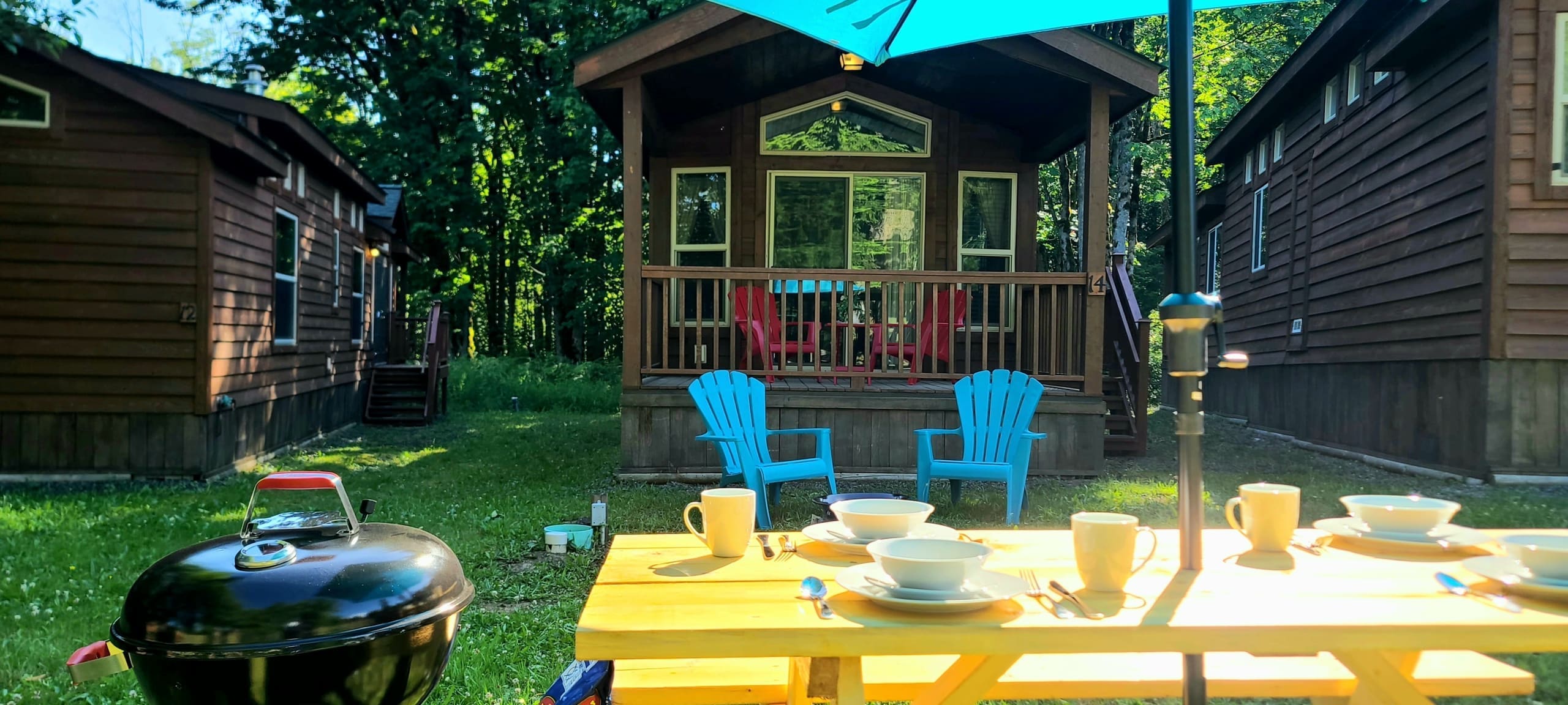 Glamping picnic table with dishes and kettle BBQ in front of cabin 14