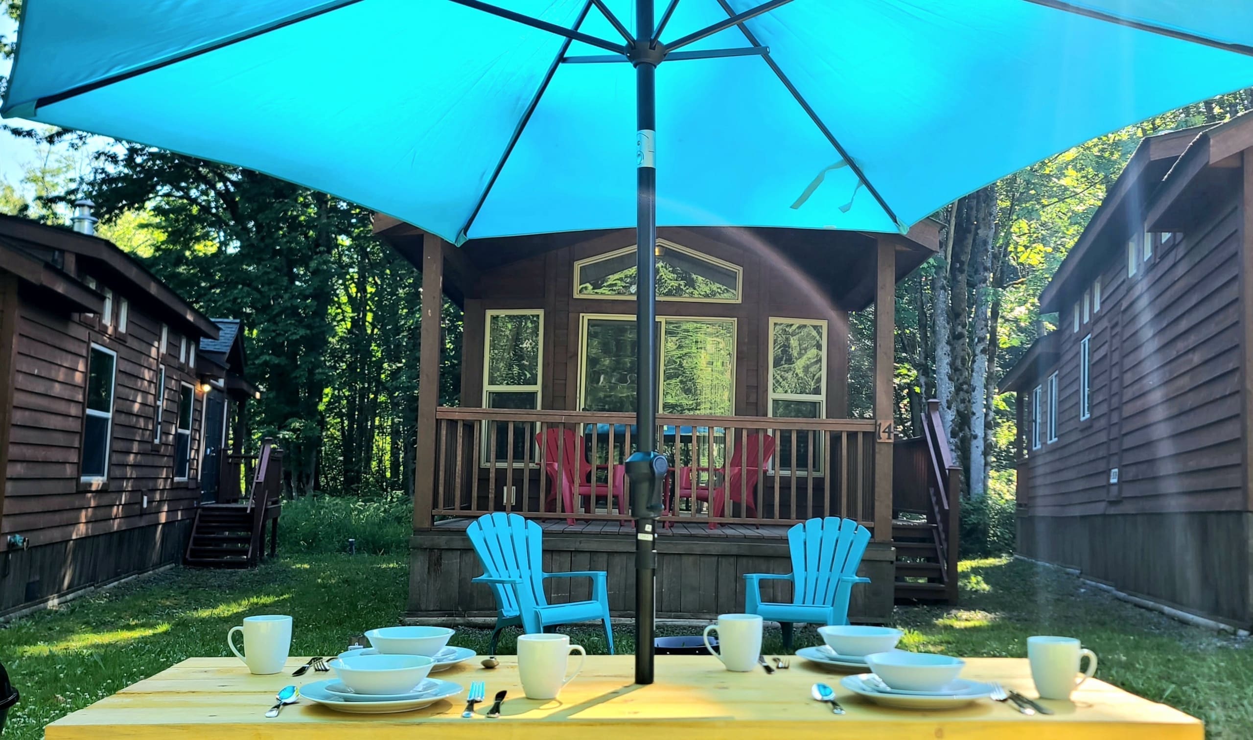 Turquoise patio umbrella shading a picnic table in front of a cabin porch