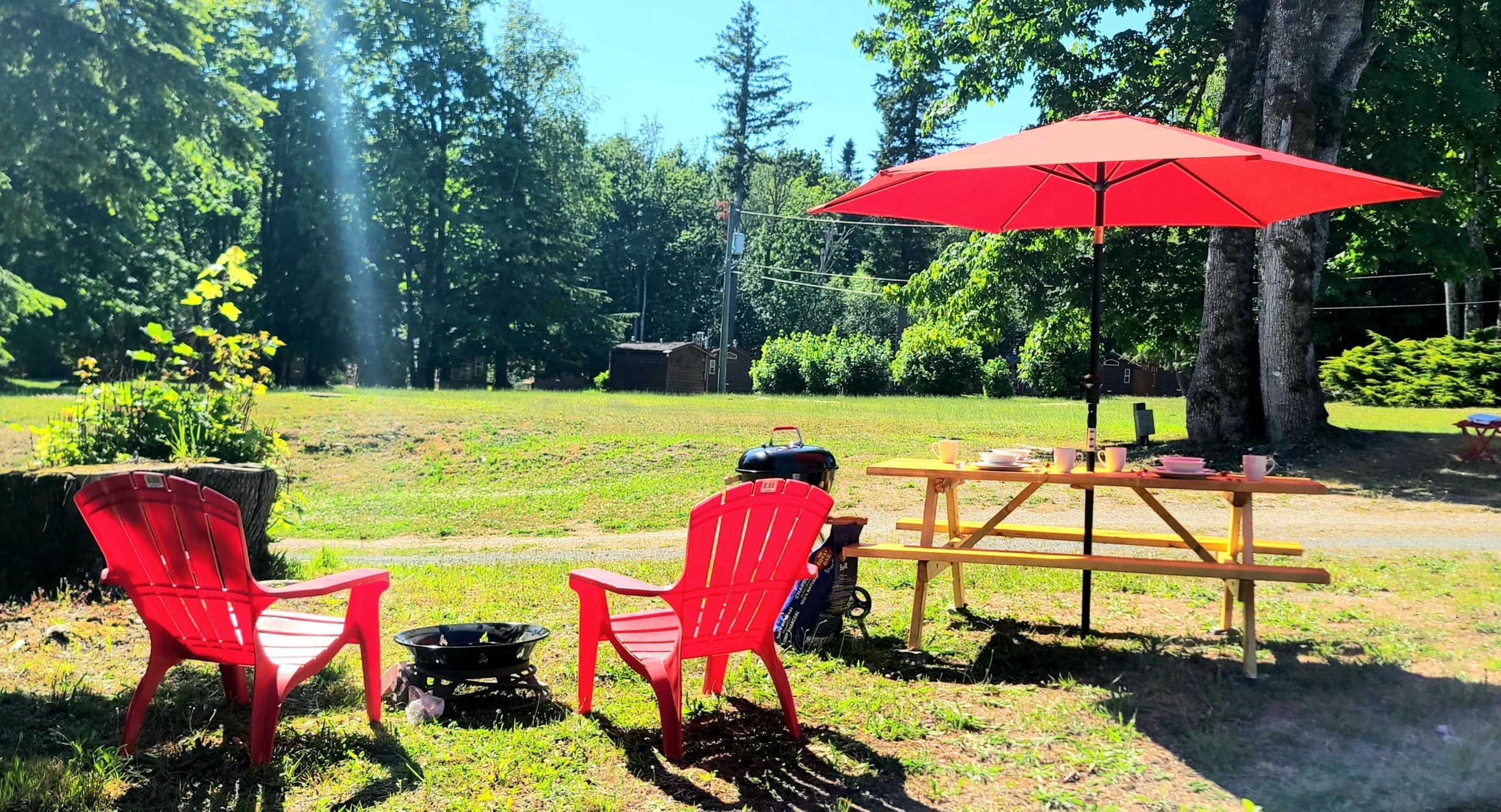 Red Adirondack chairs around a fire pit beside the glamping picnic table
