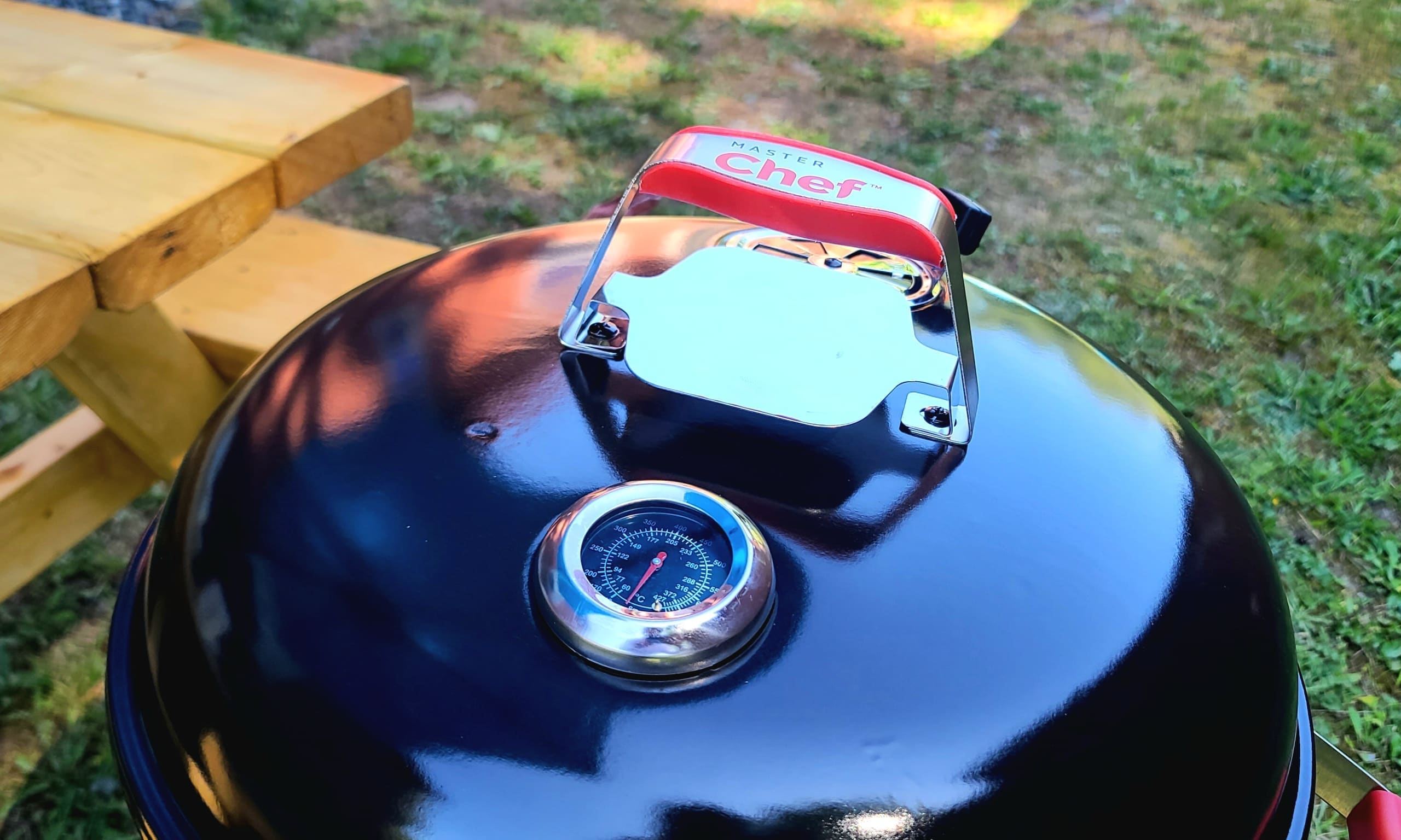 Charcoal kettle BBQ grill with thermometer beside the picnic table