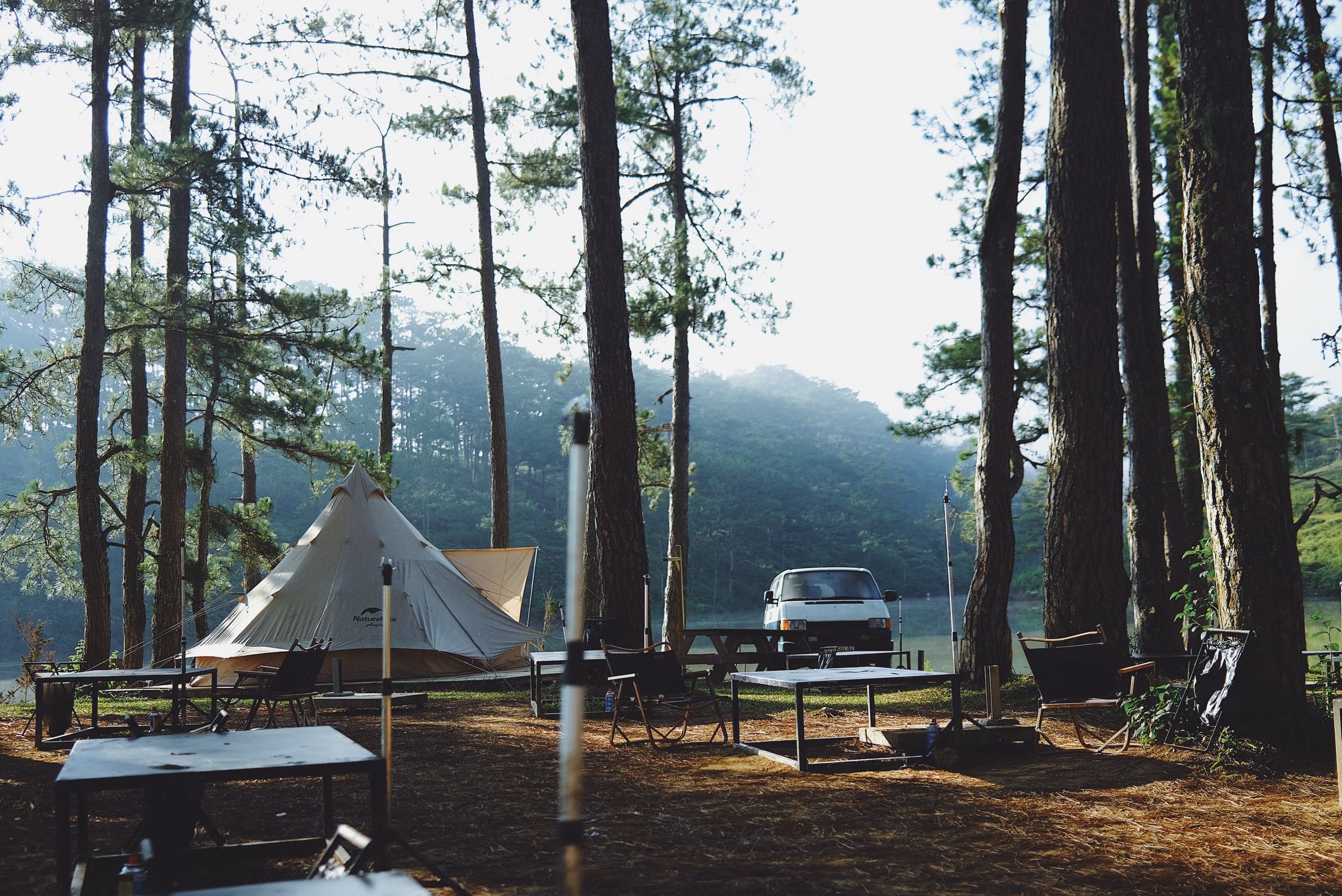 Glamping picnic tables with a blue umbrella and grill in front of the cabins