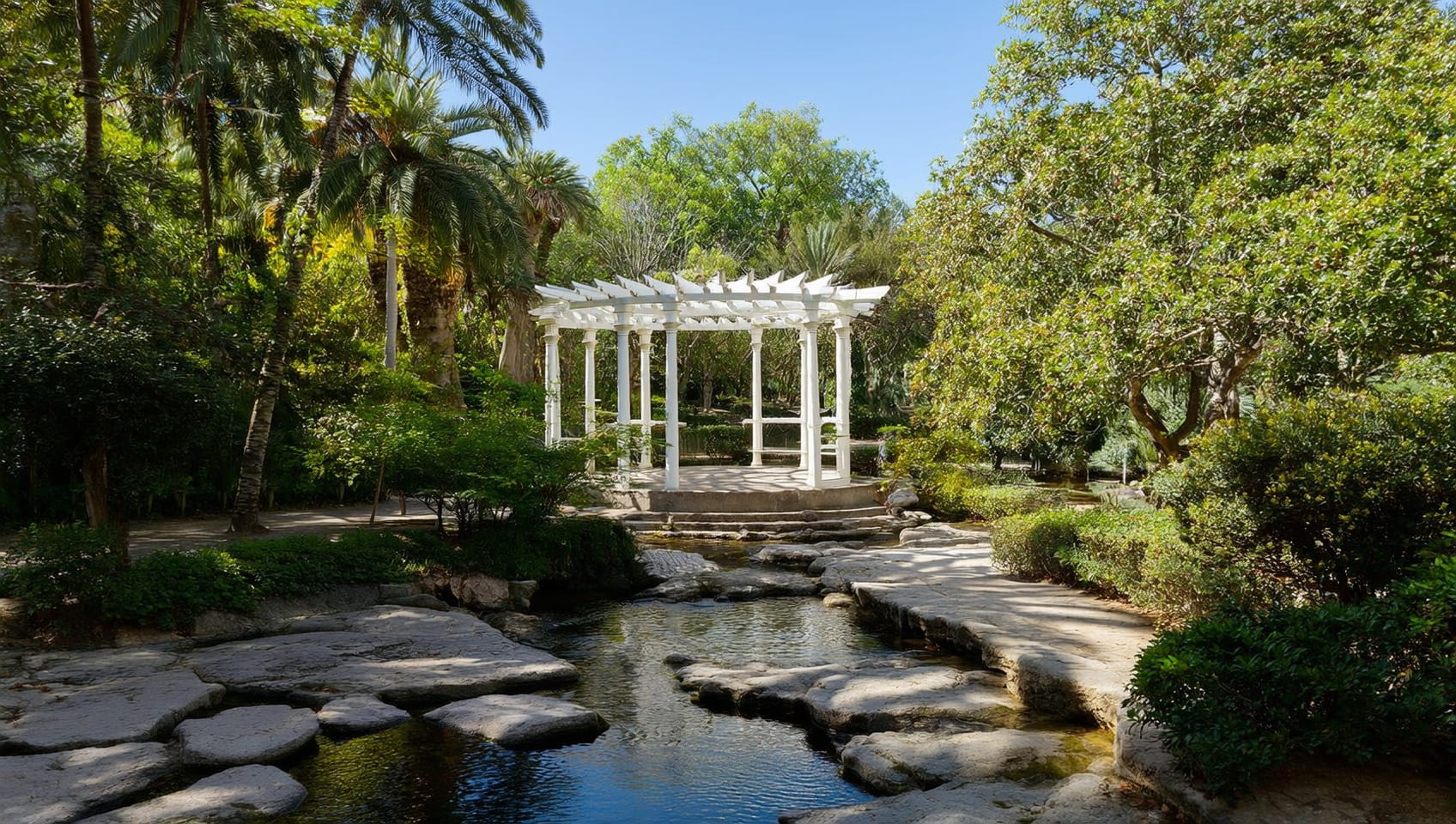 White pergola and arched footbridge over a rocky creek in the resort gardens